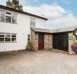 Exterior of a two story house with white walls stone entrance and black garage doors with flowers in planters at Holly Farm Cottage in Howey