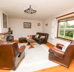 A living room with leather sofas a wooden coffee table a stone fireplace and a large window at Holly Farm Cottage in Howey
