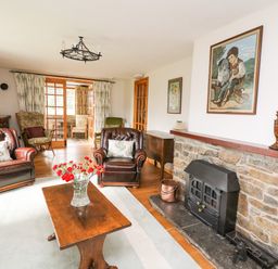 A living room with leather armchairs wooden table flowers and a stone fireplace at Holly Farm Cottage in Howey