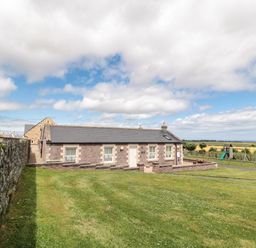 A single-storey brick house with windows and a door surrounded by grass and a stone wall at Grey Croft in Embleton