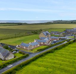 A rural landscape with stone buildings near a road and fields extending to the coastline at Grey Croft in Embleton