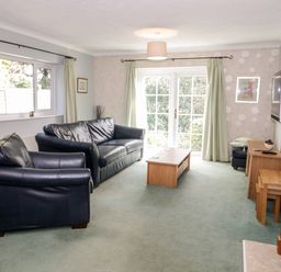 A living room with black leather sofas a wooden coffee table a wall-mounted television and French doors at Treetops in Rhos-On-Sea