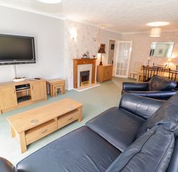 A living room with black leather sofas a wooden coffee table a wooden TV stand flat screen TV fireplace and a dining table with chairs at Treetops in Rhos-On-Sea