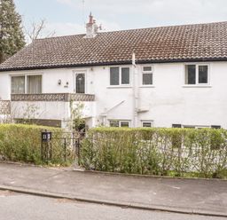 A two story white house with a tiled roof surrounded by trees and a hedge at Treetops in Rhos-On-Sea