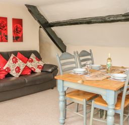 A dining table set for four beside a sofa with cushions under a sloped ceiling with black beams at Fig Trees - Wibble Farm in Williton near Watchet