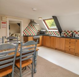 A kitchen and dining area with wooden cabinets a dining table with chairs and colorful tiled backsplash at Fig Trees - Wibble Farm in Williton near Watchet