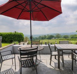 An outdoor patio with tables chairs and a red umbrella overlooking fields and trees at Aberdauddwr in Lampeter