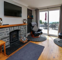 A living room with a stone fireplace a mounted TV black leather chairs and a sliding glass door to a patio at Aberdauddwr in Lampeter
