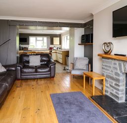A living room with leather sofas a wooden floor a stone fireplace and a view into a kitchen at Aberdauddwr in Lampeter