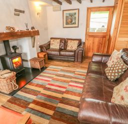 A living room with leather sofas a wood burning stove and a striped rug at Rosemary Cottage in Clawthorpe near Burton-in-Kendal