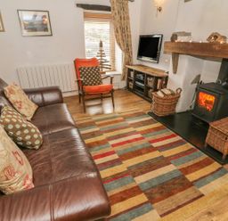 A living room with a leather sofa an armchair a wood burning stove and a patterned rug at Rosemary Cottage in Clawthorpe near Burton-in-Kendal