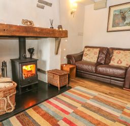 A living room with a wood-burning stove basket of logs leather sofa and framed deer picture at Rosemary Cottage in Clawthorpe near Burton-in-Kendal