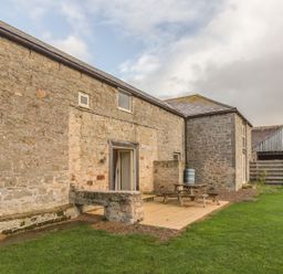 Stone building with small windows and patio with picnic table next to grass at Mill House in Lowick