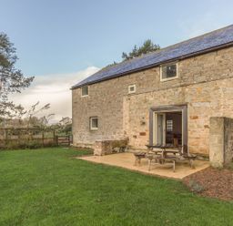 A stone building with a tiled roof and outdoor picnic table on a patio surrounded by grass at Mill House in Lowick