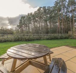 A wooden round table with attached benches on a tiled patio overlooking a grassy yard and trees at Mill House in Lowick