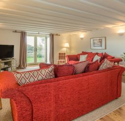 A living room with red sofas a television on a stand and glass doors at Mill House in Lowick