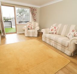 A living room with a sofa armchair a floor lamp and a door opening to an outdoor stone wall at Bryn Y Don Cottage in Benllech