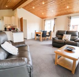A living room with two leather sofas a wooden coffee table and a dining table with chairs at Callow Lodge 5 in Beaconsfield Holiday Park