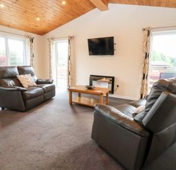 A living room with two leather sofas a wooden coffee table a wall-mounted television and large windows at Callow Lodge 5 in Beaconsfield Holiday Park