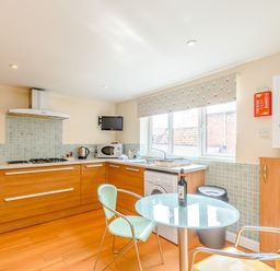 A kitchen with wooden cabinets a glass table two chairs a washing machine microwave and a window at Mermaid Cottage in Whitby