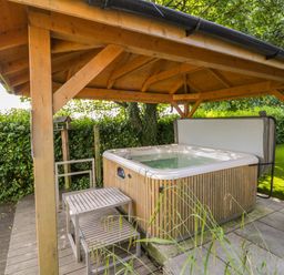 An outdoor hot tub under a wooden gazebo with steps beside it and greenery surrounding the area at Eden Lodge in Bardsea