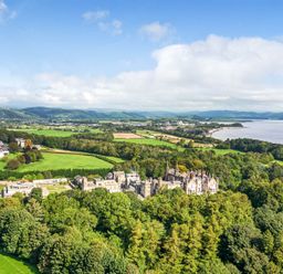 An aerial view of a large estate with a historic building surrounded by trees and fields near a body of water at Eden Lodge in Bardsea