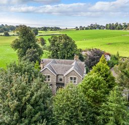 A stone house surrounded by trees and green fields at Eden Lodge in Bardsea