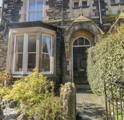 A stone house exterior with an arched doorway and bay window surrounded by bushes and a metal gate at 48 Oak Street in Windermere