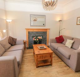 A living room with two sofas a wooden coffee table a fireplace with flowers and lamps at 48 Oak Street in Windermere