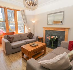 A living room with two sofas a wooden coffee table a fireplace with flowers and a large window at 48 Oak Street in Windermere