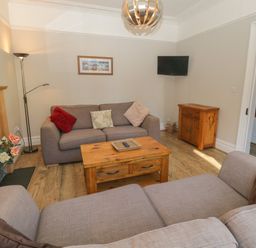 A living room with two sofas a wooden coffee table a floor lamp and a small wooden cabinet at 48 Oak Street Windermere