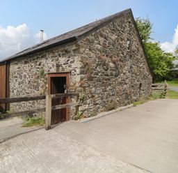 An exterior view of a stone barn with a wooden door a wooden railing and a driveway at Meader Barn Peter Tavy near Tavistock