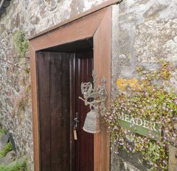 A wooden door with a metal bell and a green sign reading Meader on a stone wall at Meader Barn Peter Tavy near Tavistock