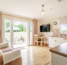 A living area with a sofa table and chairs next to kitchen counters and patio doors at Norbank Garden Studio in Bressingham