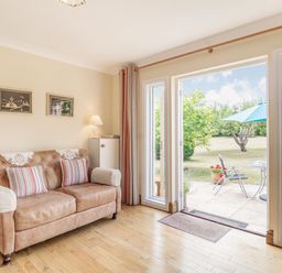 A living room with a sofa pillows and framed pictures next to glass doors leading to a garden at Norbank Garden Studio in Bressingham