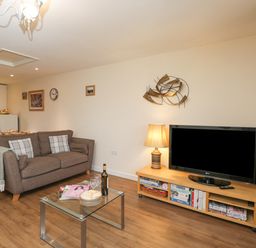 A living room with a brown sofa a glass coffee table with plates glasses and a wine bottle a wooden TV stand with a TV and a lamp at Roan Cottage in Royal Wootton Bassett
