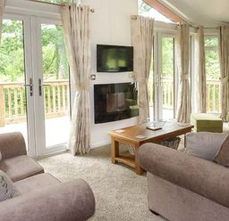 A living room with sofas a wooden coffee table a wall mounted television and glass doors at Chaffinch Lodge in Highampton near Sheepwash