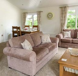A living room with two brown sofas a wooden coffee table and a dining table with chairs at Chaffinch Lodge in Highampton near Sheepwash