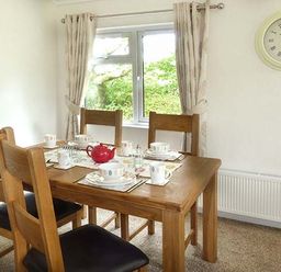 A dining room with a wooden table set for tea with cups and a red teapot at Chaffinch Lodge in Highampton near Sheepwash
