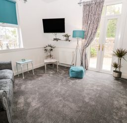 A sitting room with two sofas a TV chair floor lamp and French doors at St Cuthberts Cottage in Beal near Holy Island