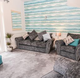 A living room with gray sofas cushions a lamp plant and glass doors at St Cuthberts Cottage in Beal near Holy Island