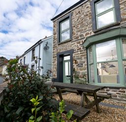 Exterior view of a stone cottage with green windows and door and a wooden picnic table in front at Rose Cottage in St Dogmaels near Cardigan