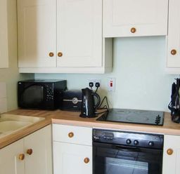 A kitchen with white cabinets wooden knobs a microwave toaster kettle utensils and an oven at The Beach House Apartment in Buncrana County Donegal