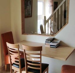 A dining area with a wooden table attached to the wall two wooden chairs and two red upholstered chairs near a window with a mirror above the table at The Beach House Apartment in Buncrana County Donegal
