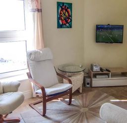 A living room with two armchairs a round glass side table a wall-mounted television and a wooden media unit at The Beach House Apartment in Buncrana County Donegal