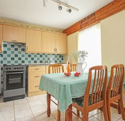 A kitchen with wooden cabinets and a tiled backsplash with a table covered by a green checkered tablecloth and wooden chairs at 4 Manorcombe  Honicombe Manor near Gunnislake