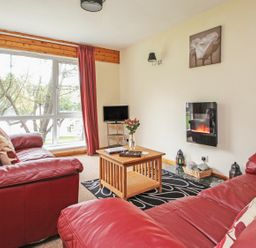 A living room with red leather sofas a wooden coffee table and a wall-mounted electric fireplace at 4 Manorcombe Honicombe Manor near Gunnislake