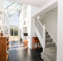 A hallway with staircase carpeted stairs and wooden furniture next to glass wall and door at 1 Atlantic Haven in Llangennith