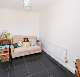 A small room with a beige sofa with cushions a wooden shelf with toys a radiator and a small television on a wooden stand at 1 Atlantic Haven in Llangennith