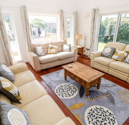 A living room with two cream sofas one beige sofa wooden coffee table and large windows at 1 Atlantic Haven in Llangennith